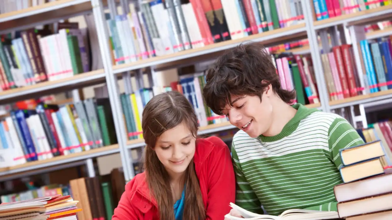 Dwoje uczniów czytających książki przy stole w bibliotece — zdjęcie ilustracyjne