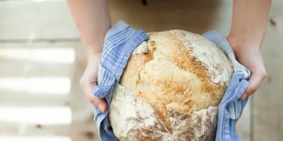 Bochenek chleba trzymany w dłoniach przez ściereczkę — zdjęcie ilustracyjne